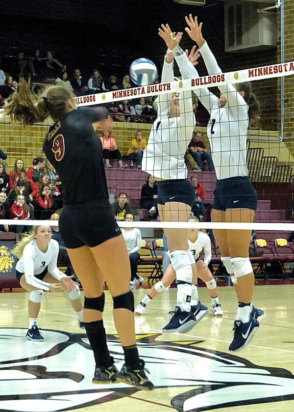 UMD's Sarah Kelly drilled a kill past Concordia's Sydney Book and Hope Schiller (right) during the first game of the 3-1 Bulldogs victory at Romano Gym. Photo credit: John Gilbert