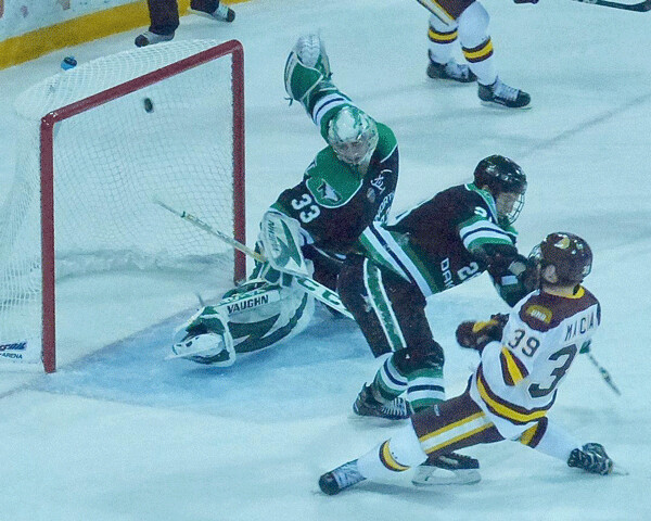 UMD’s Parker Mackay absorbs a bodycheck from North Dakota’s Hayden Shaw in order to get  his shot off, just under the crossbar... Photo credit: John Gilbert