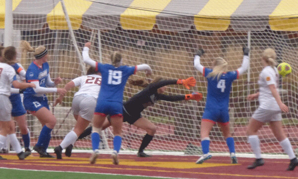 Mary midfieldeer Megan Lowery (13 blue) redirected a corner kick just out of the reach of diving UMD goalkeeper Carlye Wright in the 86th minute, for a 1-0 victory that ultimately left the Bulldogs just shy of the eighth and final NSIC playoff spot. Photo credit: John Gilbert