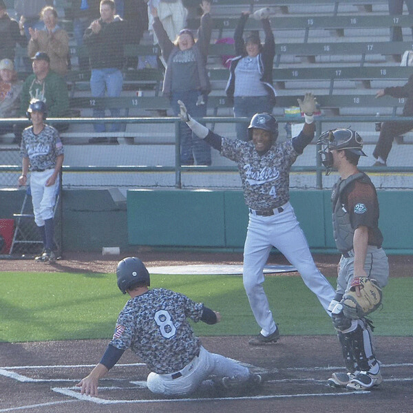 Trailing 7-5 with two out in last of ninth in the Huskies home opener, General McArthur IV scores the tying run then turns to signal Cade Edwards to slide home with the winning run. Photo credit: John Gilbert