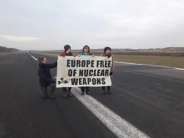 Three Members of the European Parliament climbed into the Kleine Brogel air force base in Belgium February 20 and symbolically blocked the runway, demanding the withdrawal of the US nuclear bombs stationed there. Standing with banner L-to-R were lawmakers Molly Scott Cato,  Tilly Metz, and Michèle Rivasi. Photo by Act for Peace.