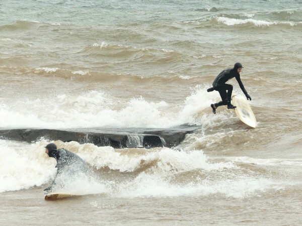 A surfer decided to leave his rocky spot in Lake Superior while another rode a wave past him, then he decided to join him and made a fairly awkward  leap into the frigid water near Lester River for a 1-second ride. Photo credit: John Gilbert