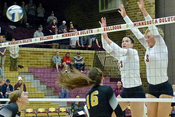 Allison Olley (13) and Taylor Wissbroecker blocked Alex Opperman;s attempt as UMD won the first two sets of their NSIC playoff match. Photo credit: John Gilbert